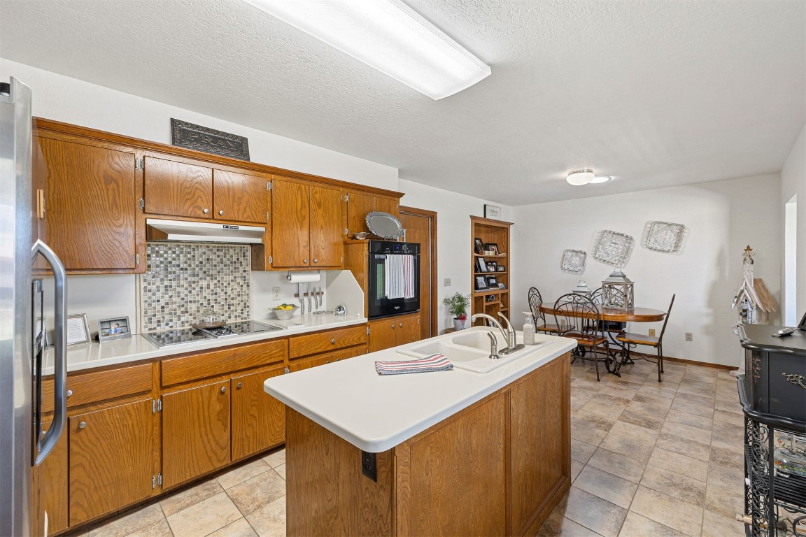 1524 W Oak Street, El Reno, OK 73036 kitchen with tasteful backsplash, a kitchen island with sink, black appliances, and light tile floors