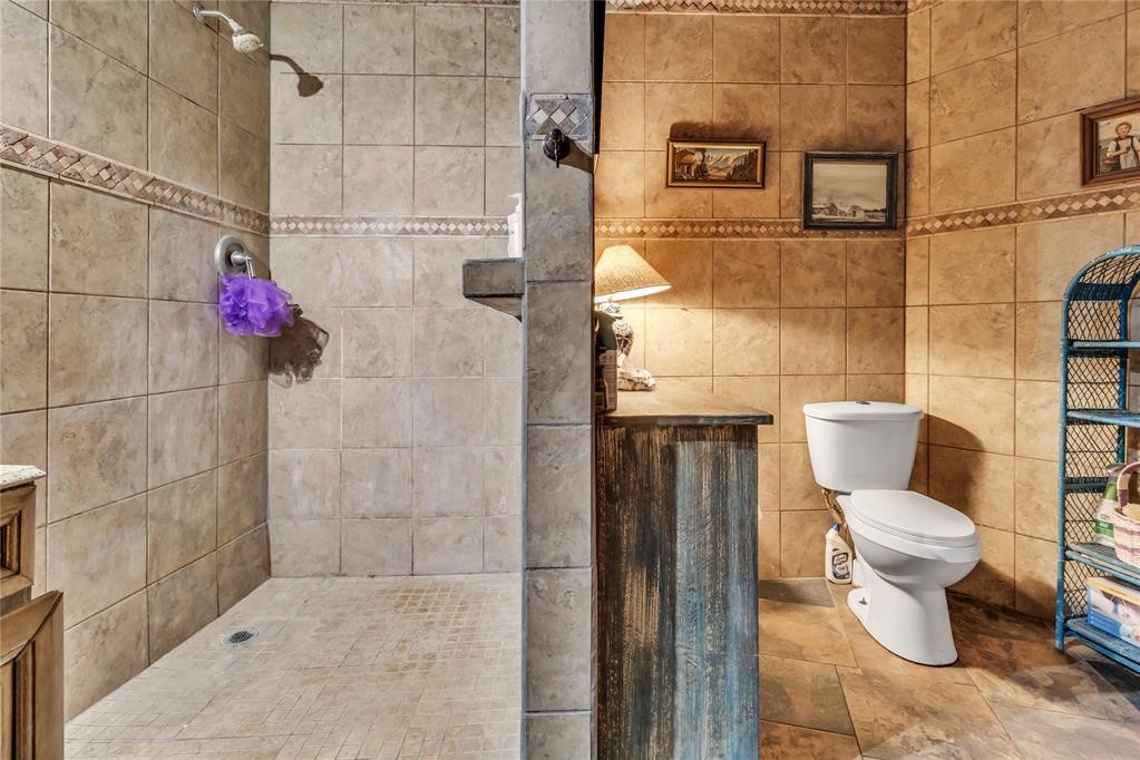 7676 W County Road 66, Mulhall, OK 73063 bathroom featuring tiled shower, tile floors, vanity, tile walls, and toilet