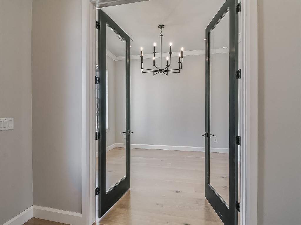 2201 Pallante Street, Edmond, OK 73034 corridor featuring french doors, an inviting chandelier, crown molding, and light wood-type flooring