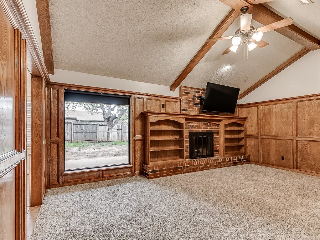 1521 NE 3rd Street, Moore, OK 73160 unfurnished living room featuring a brick fireplace, a textured ceiling, vaulted ceiling with beams, light colored carpet, and built in features