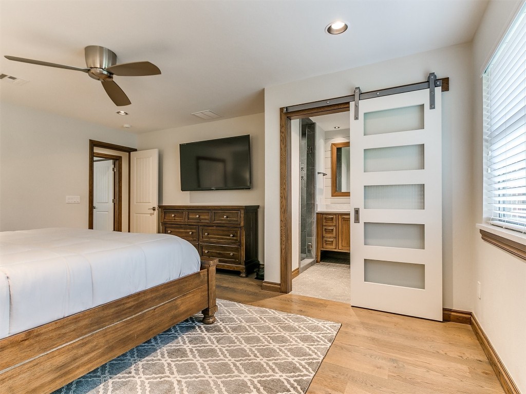 609 S Chloe Lane, Mustang, OK 73064 bedroom featuring ensuite bathroom, ceiling fan, a barn door, and light wood-type flooring