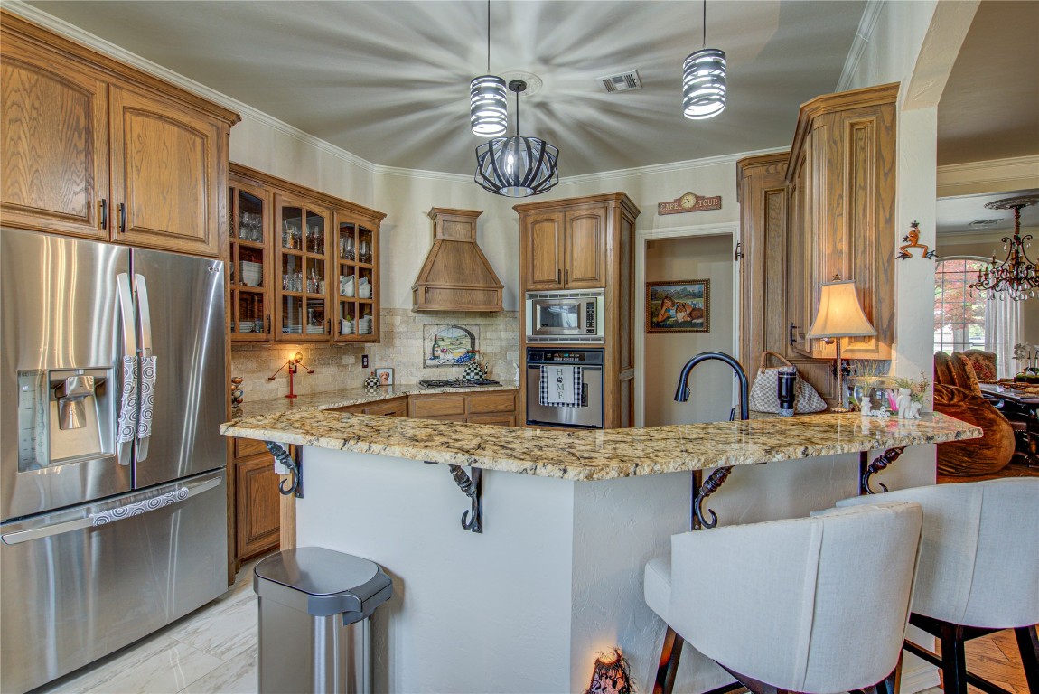 4209 Heavenfield Court, Edmond, OK 73034 kitchen featuring backsplash, a kitchen breakfast bar, appliances with stainless steel finishes, and hanging light fixtures