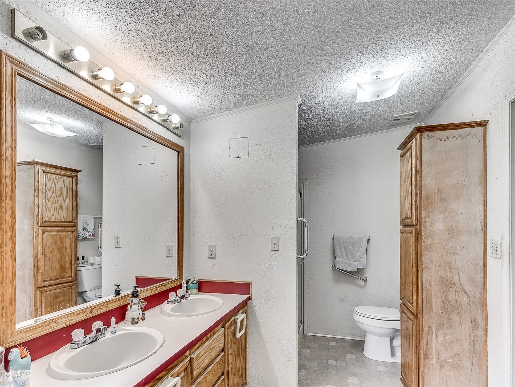 12 Galvin Drive, Guthrie, OK 73044 bathroom featuring tile floors, toilet, double sink, and a textured ceiling