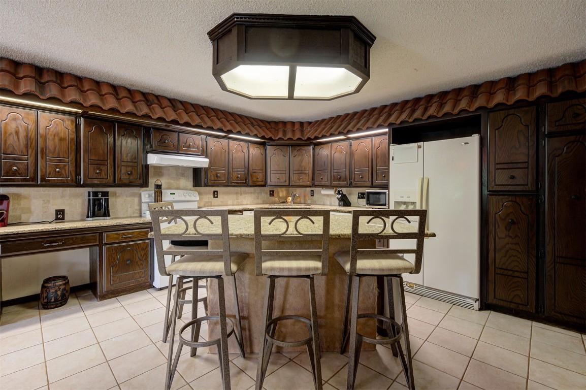 1517 S Spring Creek Drive, Mustang, OK 73064 kitchen with dark brown cabinets, white appliances, tasteful backsplash, a center island, and light tile floors