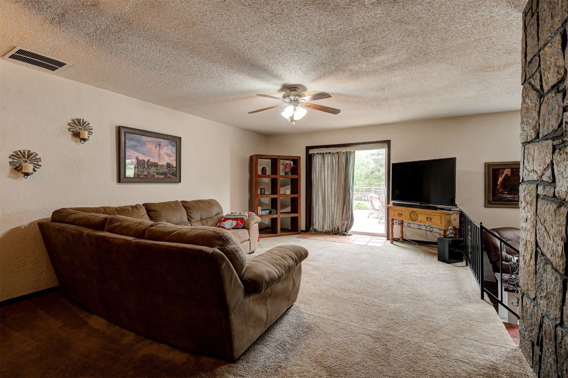 1517 S Spring Creek Drive, Mustang, OK 73064 carpeted living room featuring ceiling fan, a textured ceiling, and a fireplace