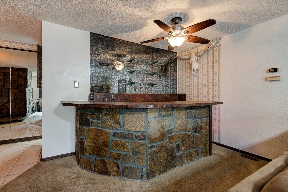1517 S Spring Creek Drive, Mustang, OK 73064 bar featuring a textured ceiling, ceiling fan, and light carpet