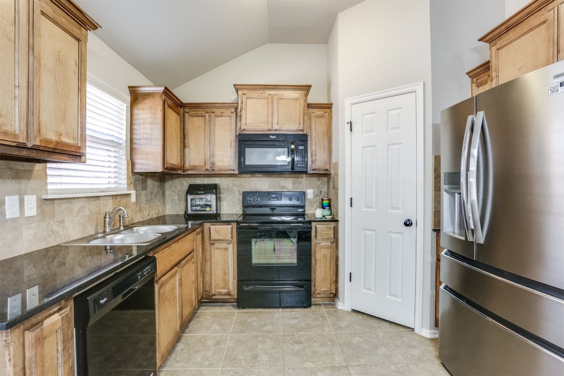 Address Hidden kitchen with backsplash, light tile flooring, black appliances, lofted ceiling, and sink