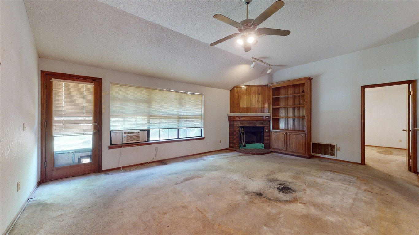 3100 SW 93rd Street, Oklahoma City, OK 73159 unfurnished living room with a textured ceiling, light carpet, vaulted ceiling, and a fireplace