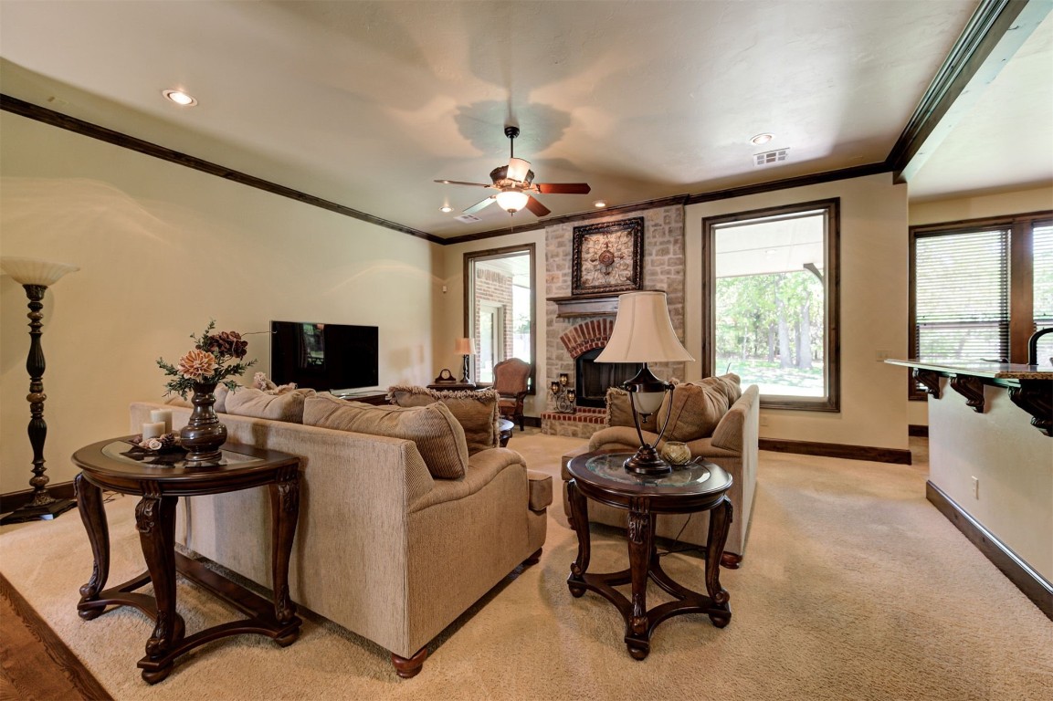 2123 Estancia Circle, Edmond, OK 73034 living room featuring light colored carpet, ornamental molding, ceiling fan with notable chandelier, and a fireplace