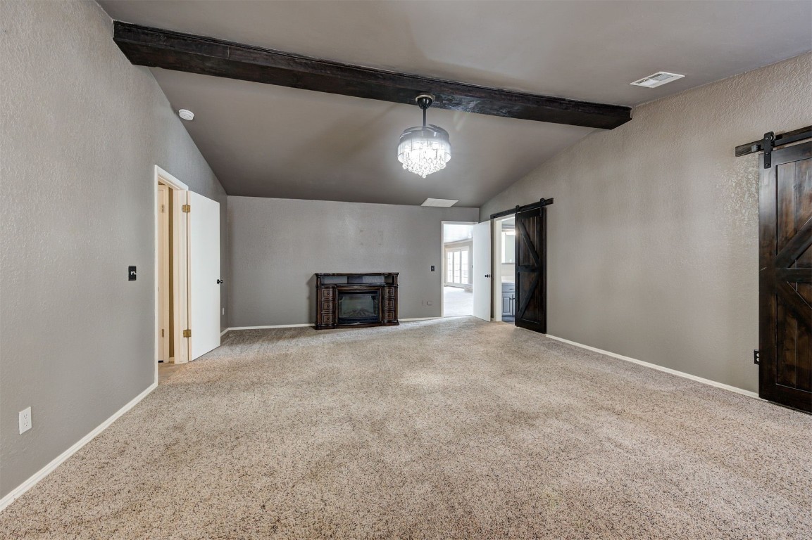 6712 Briarcreek Drive, Oklahoma City, OK 73162 unfurnished living room with light colored carpet, vaulted ceiling with beams, a chandelier, and a barn door