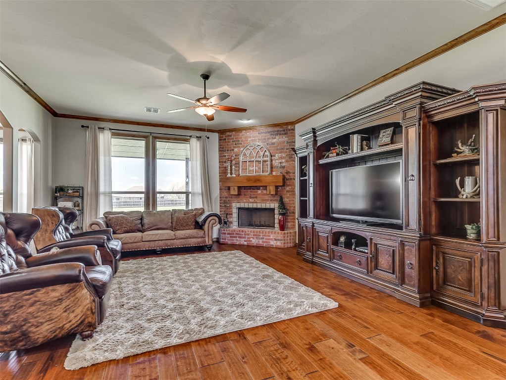 519 Harold Drive, #NE, Piedmont, OK 73078 living room with ceiling fan, a fireplace, brick wall, ornamental molding, and wood-type flooring