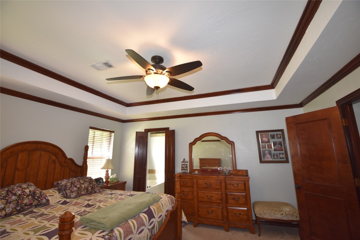 4200 Ainsley Court, Edmond, OK 73034 carpeted bedroom featuring a tray ceiling, ceiling fan, and crown molding