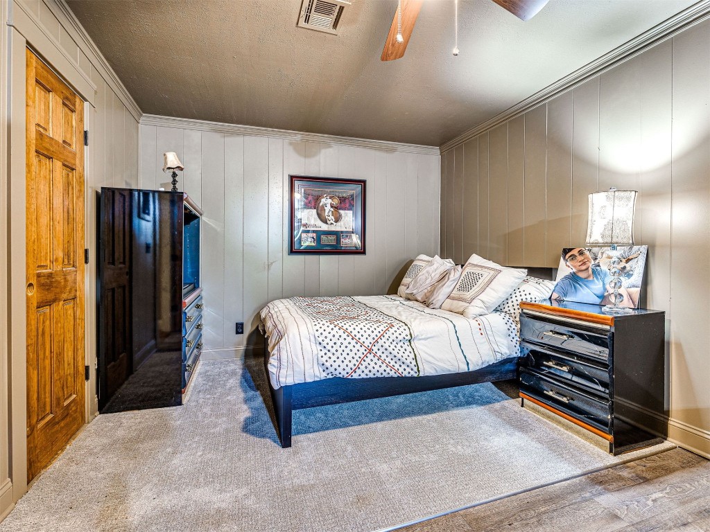 1580 NW 220th Street, Edmond, OK 73025 bedroom with crown molding, wood walls, wood-type flooring, and ceiling fan