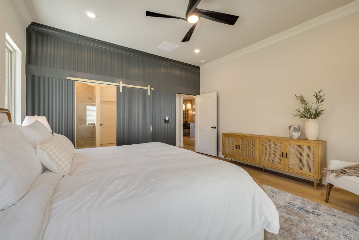 303 E 4th Street, Edmond, OK 73034 bedroom featuring ceiling fan, crown molding, light wood-type flooring, and a barn door