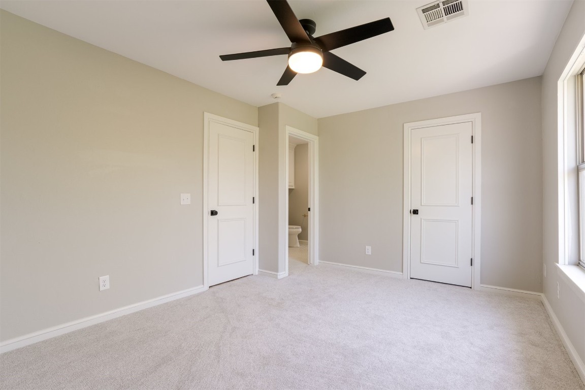 3624 Hunters Creek Road, Edmond, OK 73003 unfurnished bedroom featuring light colored carpet, ceiling fan, connected bathroom, and multiple windows