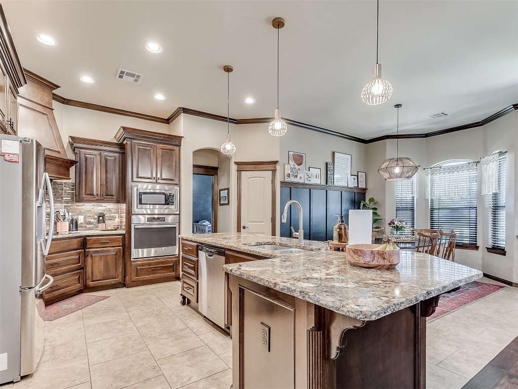 705 Evening Drive, Yukon, OK 73099 kitchen featuring hanging light fixtures, backsplash, stainless steel appliances, a kitchen bar, and a center island with sink