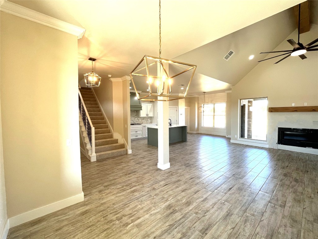 1392 S Gabes Court, Mustang, OK 73064 unfurnished living room featuring lofted ceiling with beams, sink, ceiling fan with notable chandelier, ornamental molding, and hardwood / wood-style flooring