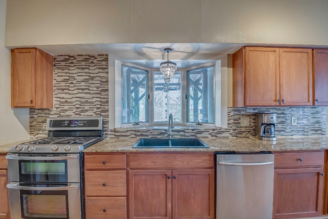 Address Hidden kitchen with light stone counters, sink, backsplash, stainless steel appliances, and pendant lighting