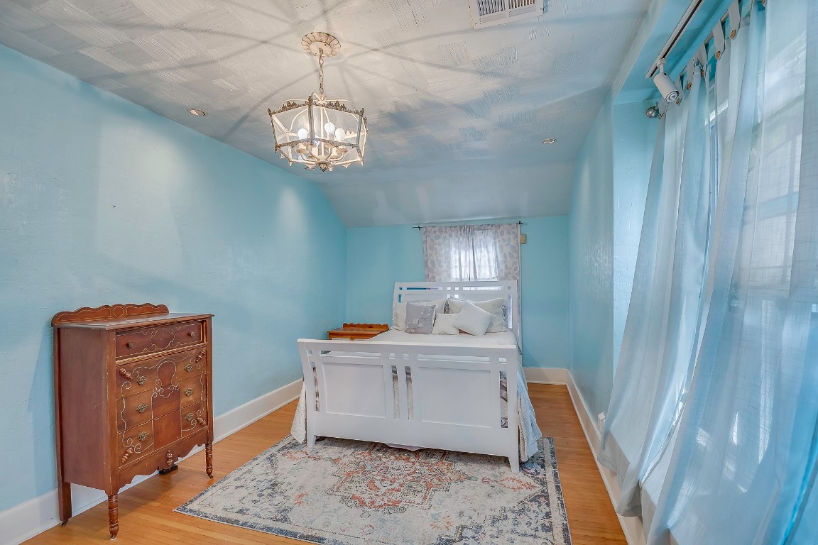 Address Hidden bedroom featuring vaulted ceiling, a notable chandelier, and light wood-type flooring