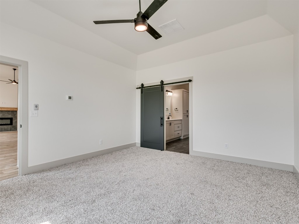 118 NE Primrose Point Avenue, Piedmont, OK 73128 unfurnished bedroom with dark colored carpet, a barn door, ceiling fan, and ensuite bathroom