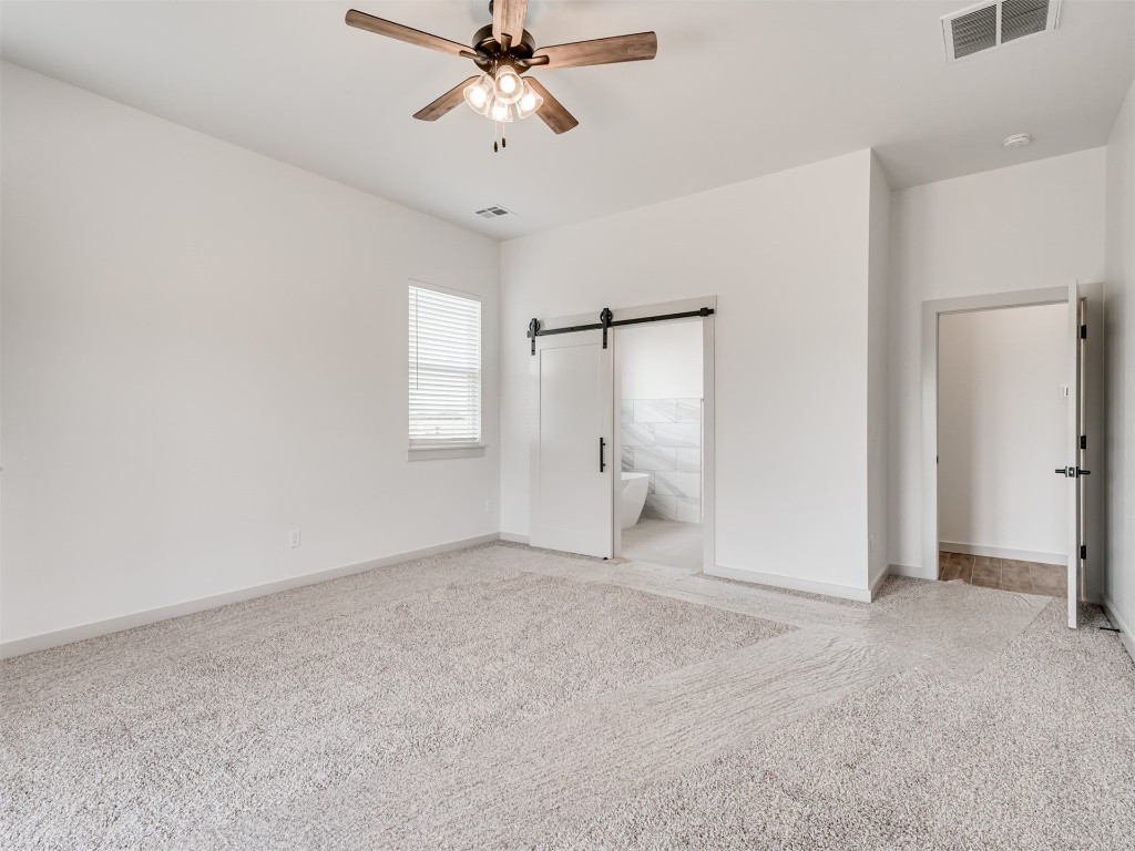 508 Venetian Avenue, Piedmont, OK 73078 unfurnished bedroom with a barn door, light carpet, ceiling fan, and ensuite bathroom