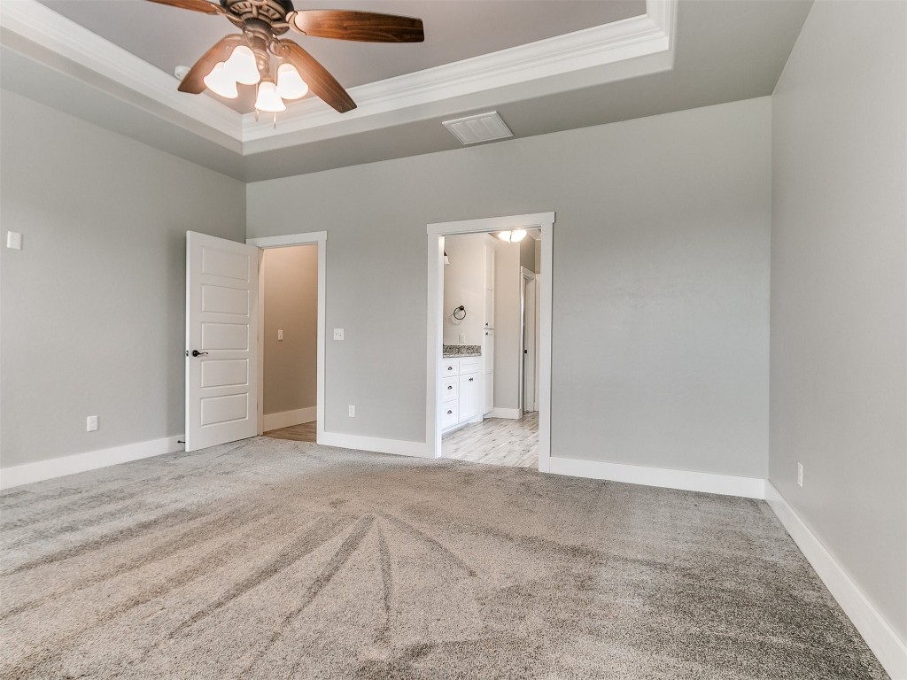 26812 Bridlewood Road, Blanchard, OK 73010 unfurnished bedroom featuring light colored carpet, ceiling fan, a raised ceiling, and ensuite bath
