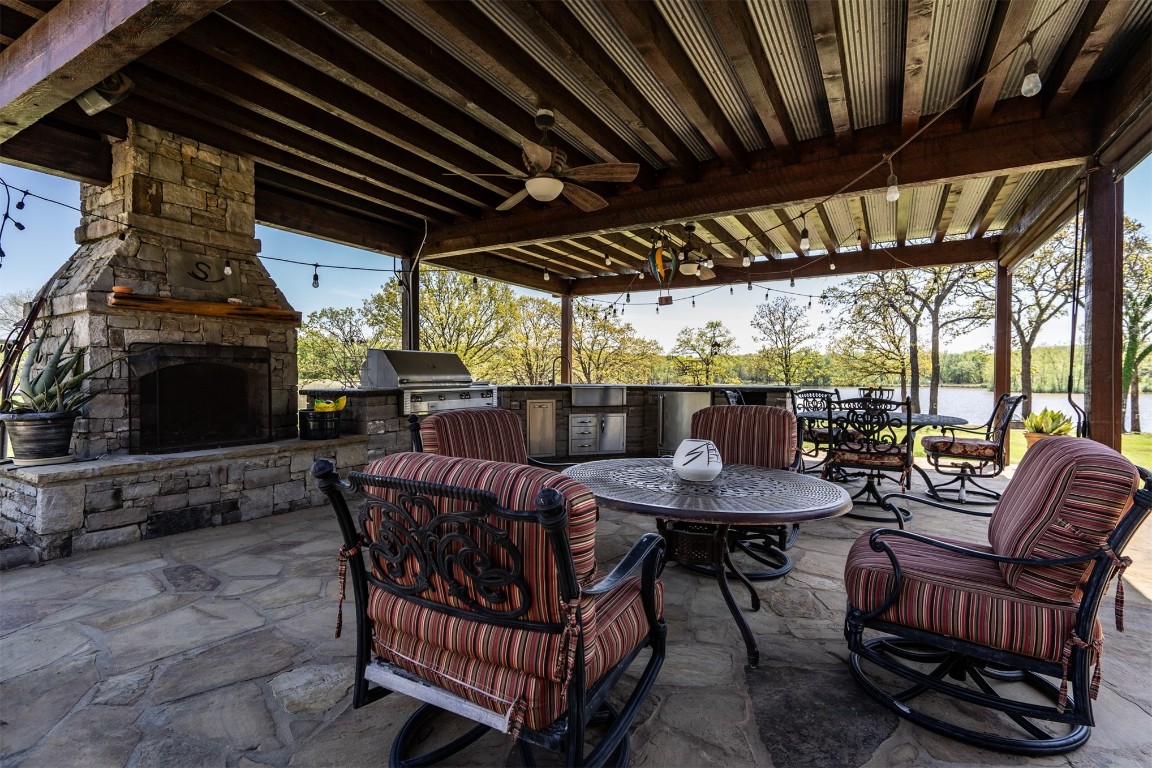 Address Hidden view of patio / terrace with ceiling fan, a water view, exterior kitchen, a grill, and an outdoor stone fireplace
