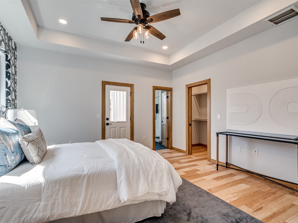 730 W Hurd Street, Edmond, OK 73003 bedroom featuring a closet, light wood-type flooring, a tray ceiling, ceiling fan, and a walk in closet