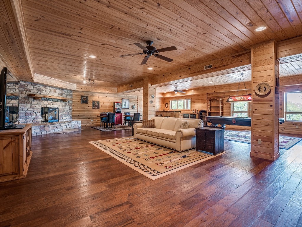 2050 S Henney Road, Guthrie, OK 73044 living room featuring ceiling fan, a stone fireplace, dark wood-type flooring, wooden walls, and wooden ceiling