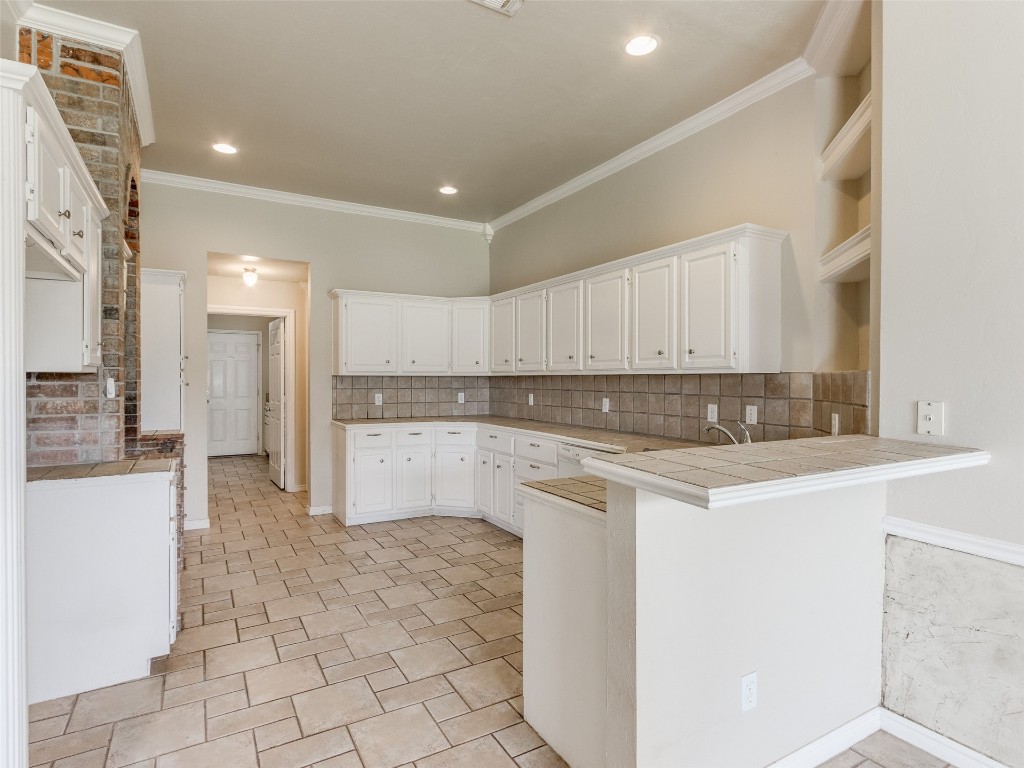 12109 Dalton Drive, Oklahoma City, OK 73162 kitchen with white cabinets, light tile flooring, backsplash, ornamental molding, and kitchen peninsula