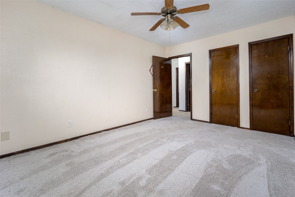 13494 290th Street, Blanchard, OK 73010 unfurnished bedroom featuring a textured ceiling, ceiling fan, carpet floors, and multiple closets