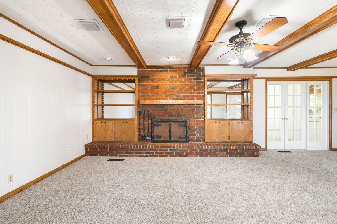 2500 S Choctaw Avenue, El Reno, OK 73036 unfurnished living room with ceiling fan, carpet flooring, a fireplace, and beam ceiling