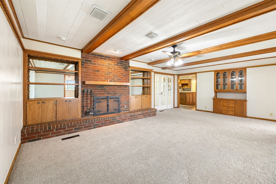 2500 S Choctaw Avenue, El Reno, OK 73036 unfurnished living room with beamed ceiling, ceiling fan, a fireplace, carpet floors, and ornamental molding
