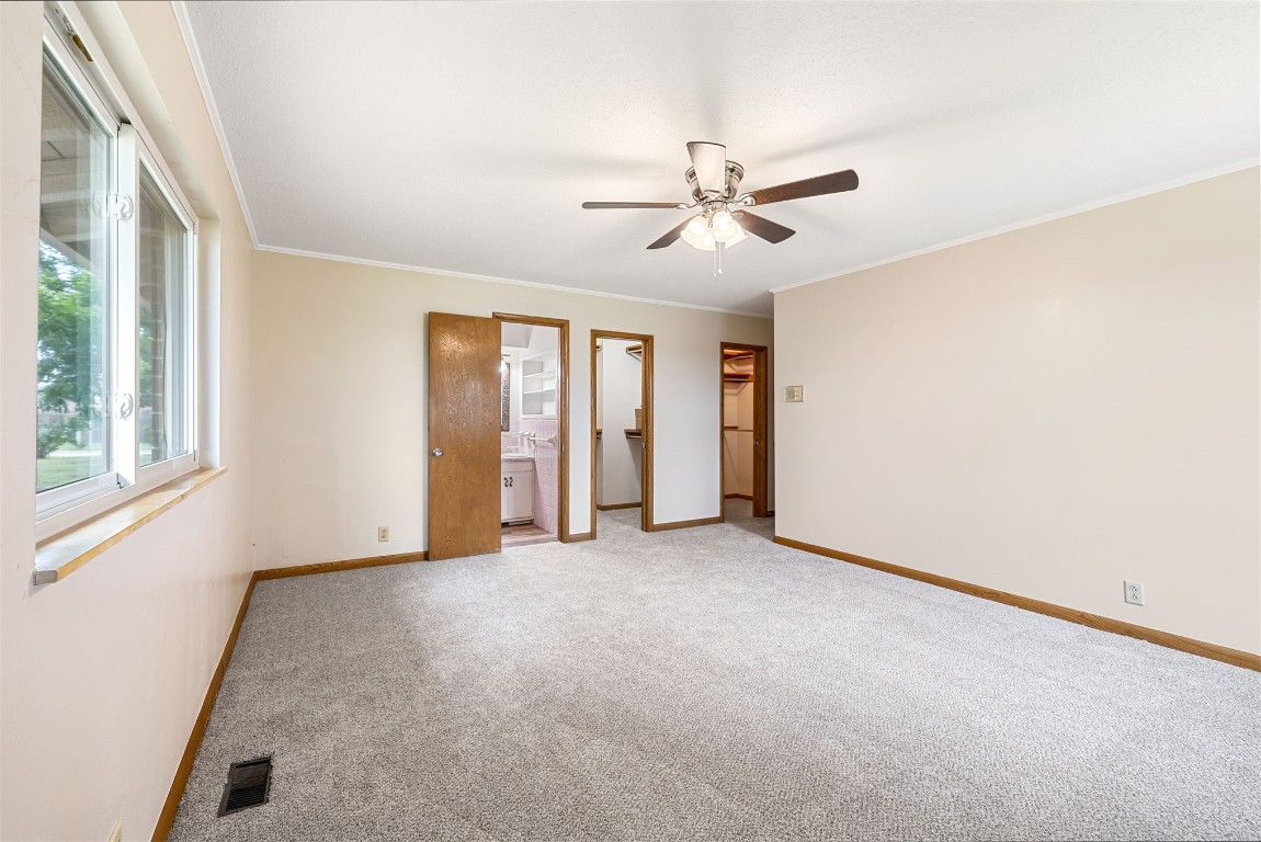 2500 S Choctaw Avenue, El Reno, OK 73036 unfurnished bedroom featuring ceiling fan, crown molding, connected bathroom, and carpet flooring