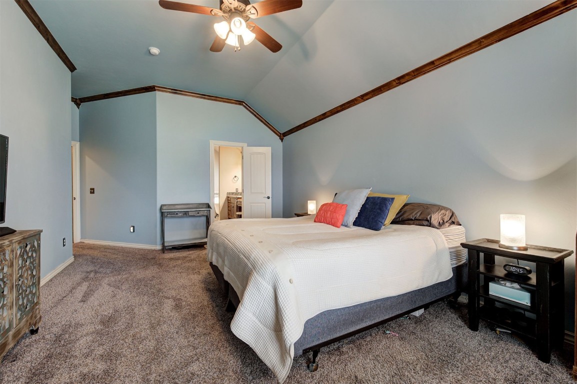 18125 Haslemere Lane, Edmond, OK 73012 carpeted bedroom featuring ceiling fan, vaulted ceiling, connected bathroom, and ornamental molding