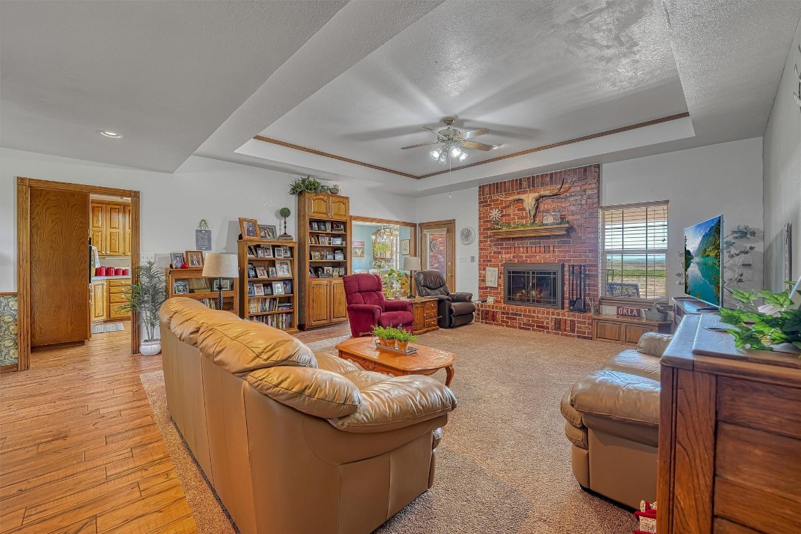 20290 E County Road 175, Elmer, OK 73539 living room with light wood-type flooring, a brick fireplace, ceiling fan, and a tray ceiling