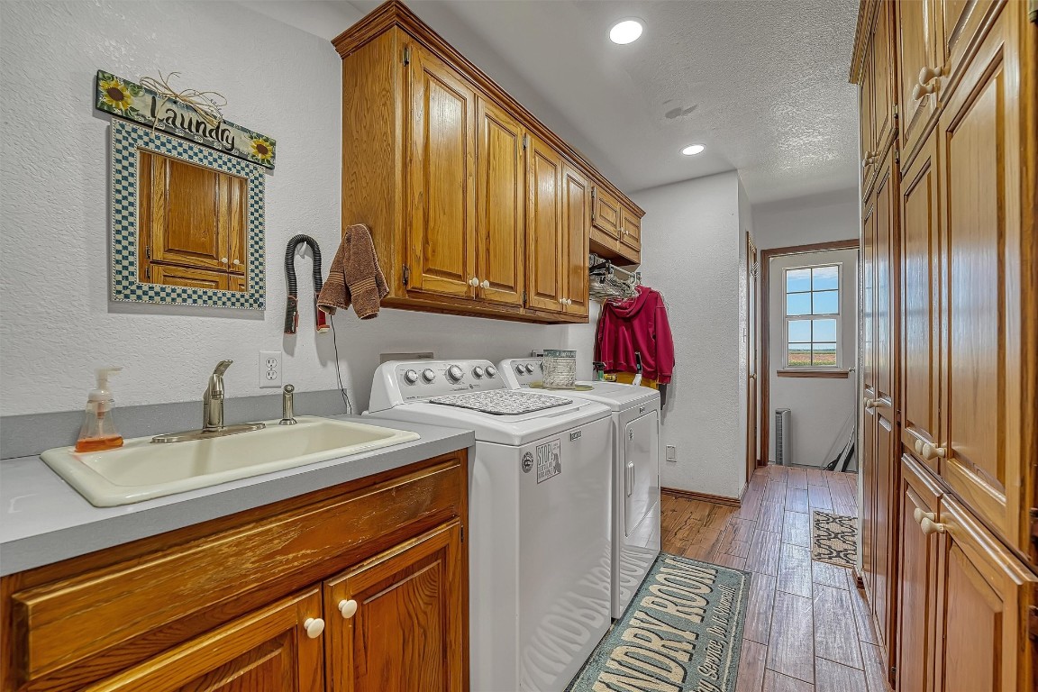 20290 E County Road 175, Elmer, OK 73539 laundry room featuring cabinets, a textured ceiling, washing machine and clothes dryer, sink, and light hardwood / wood-style floors