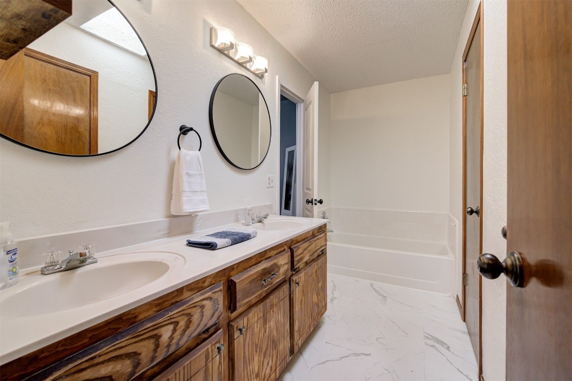 16905 Valley Lane, Edmond, OK 73012 bathroom with a bath, dual vanity, tile floors, and a textured ceiling
