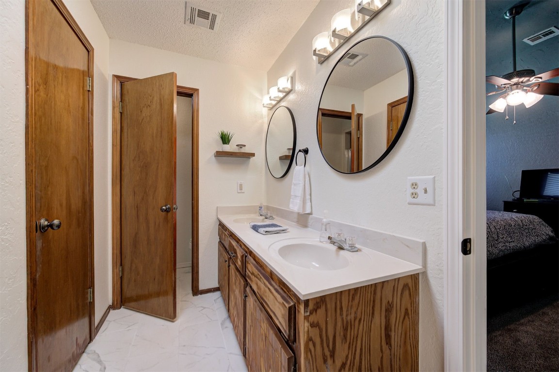 16905 Valley Lane, Edmond, OK 73012 bathroom with dual bowl vanity, tile floors, ceiling fan, and a textured ceiling