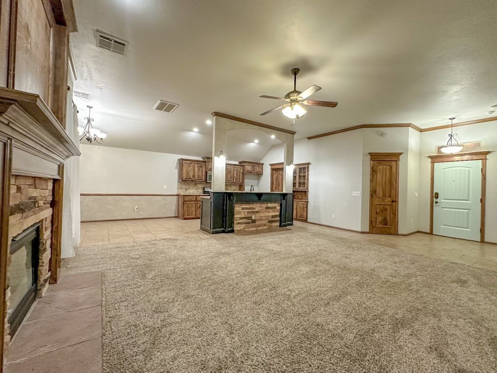 9116 NW 140th Street, Yukon, OK 73099 unfurnished living room featuring light carpet, ceiling fan with notable chandelier, ornamental molding, vaulted ceiling, and a stone fireplace