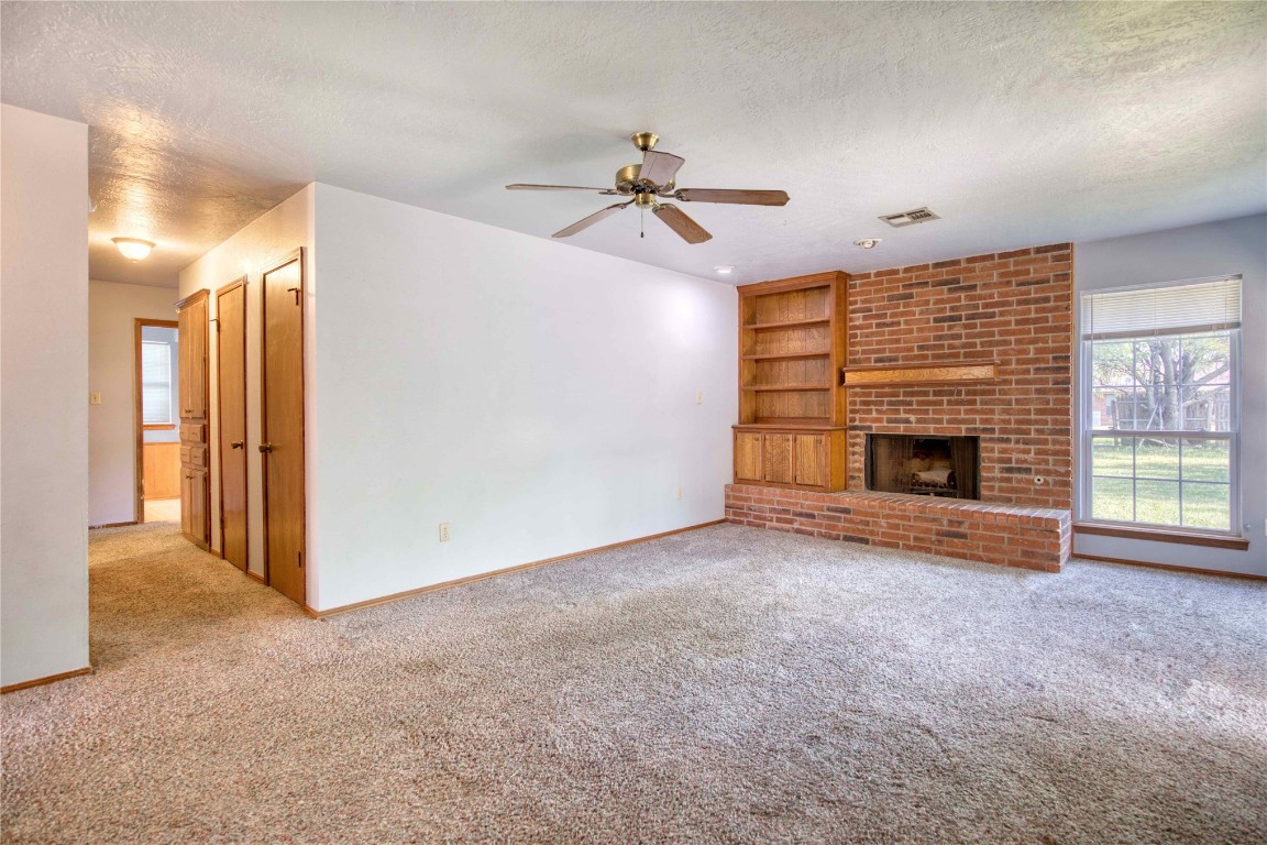 213 Falcon Court, Norman, OK 73069 unfurnished living room with brick wall, carpet, a fireplace, and a textured ceiling