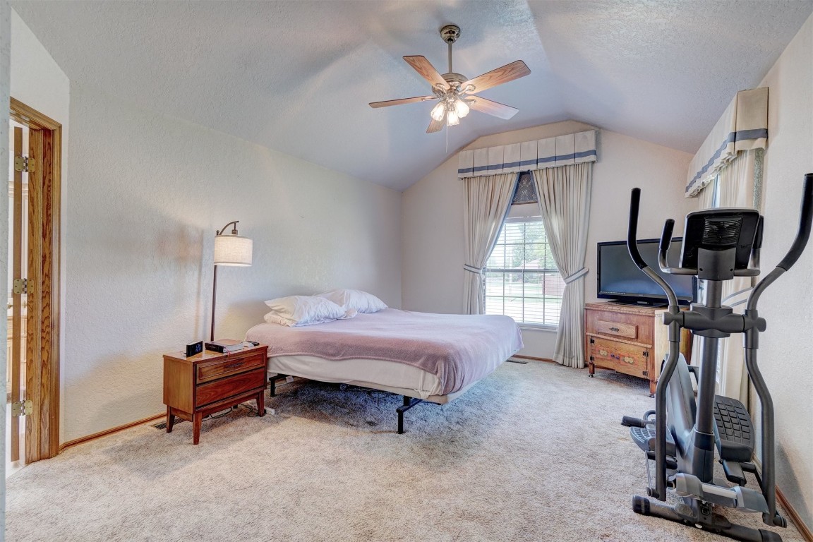 7220 NW 101st Street, Oklahoma City, OK 73162 carpeted bedroom featuring ceiling fan, vaulted ceiling, and a textured ceiling