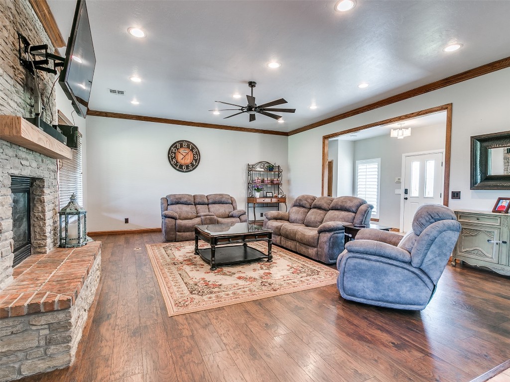 2900 Big Sky Circle, Yukon, OK 73099 living room featuring dark hardwood / wood-style floors, ceiling fan, crown molding, and a stone fireplace
