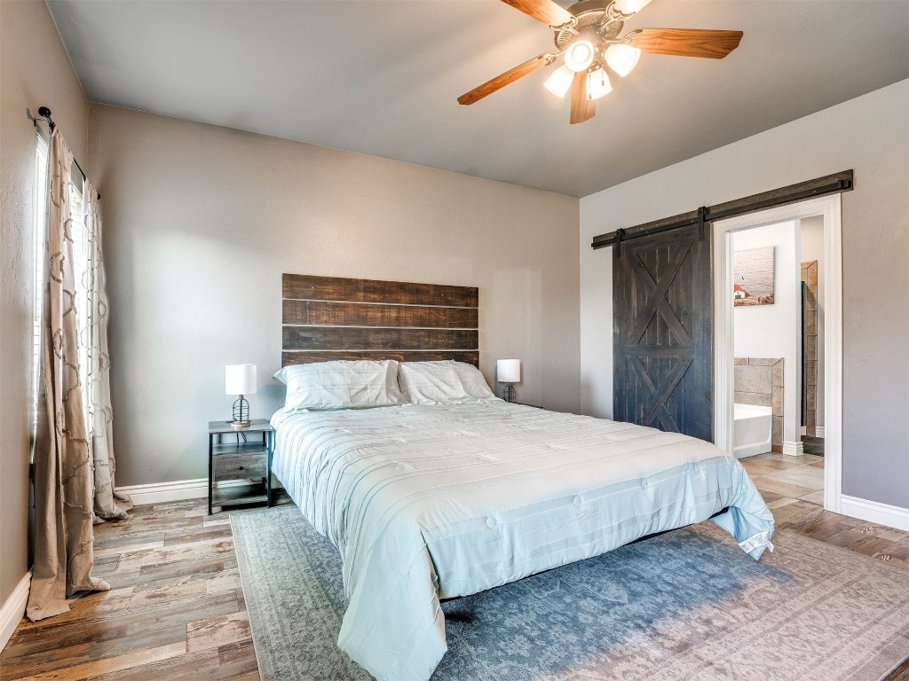 5112 SW 123rd Street, Oklahoma City, OK 73173 bedroom with a barn door, connected bathroom, ceiling fan, and hardwood / wood-style floors
