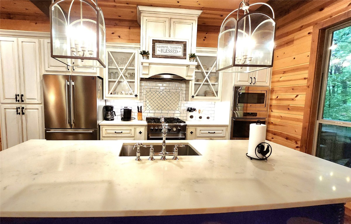 57 Mayflower Circle, Broken Bow, OK 74728 kitchen featuring wooden walls, hanging light fixtures, premium appliances, backsplash, and sink