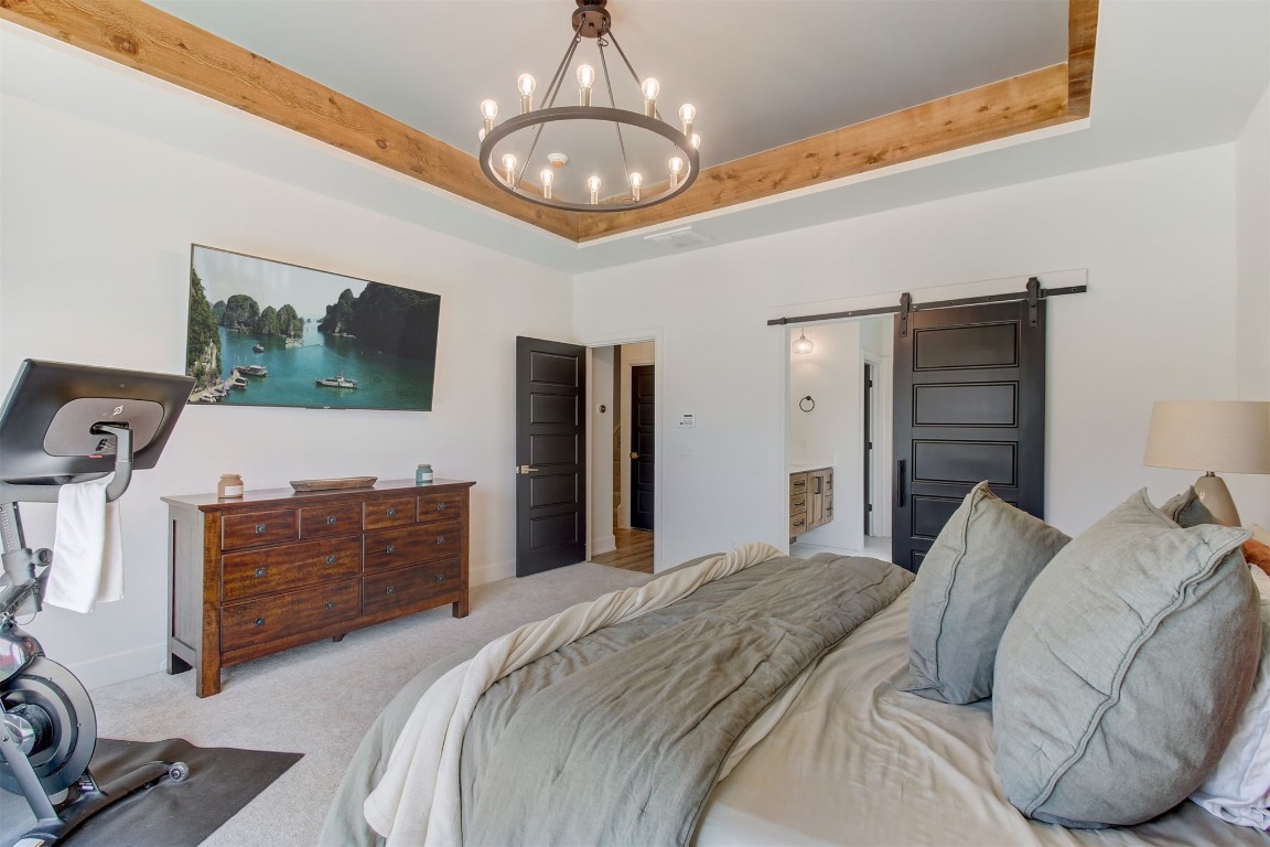 9224 NW 82nd Street, Yukon, OK 73099 carpeted bedroom featuring a raised ceiling, an inviting chandelier, and a barn door