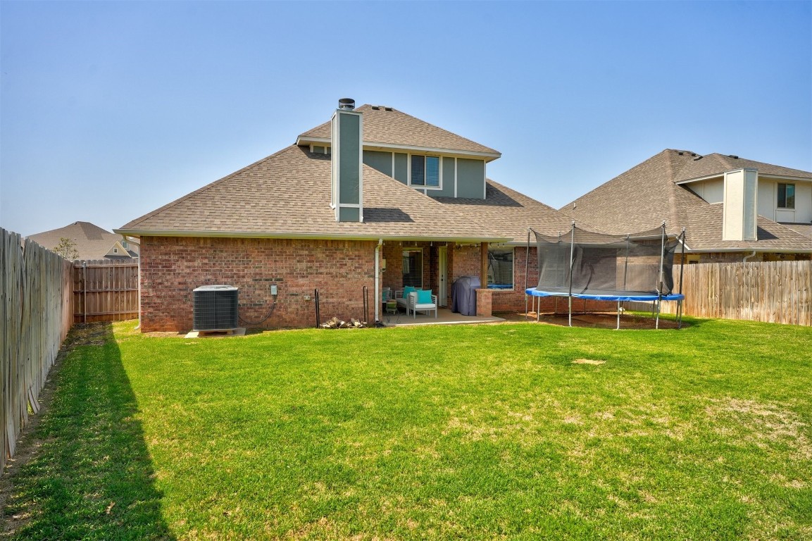 18700 Lazy Grove Drive, Edmond, OK 73012 back of house with central AC, a trampoline, a lawn, and a patio