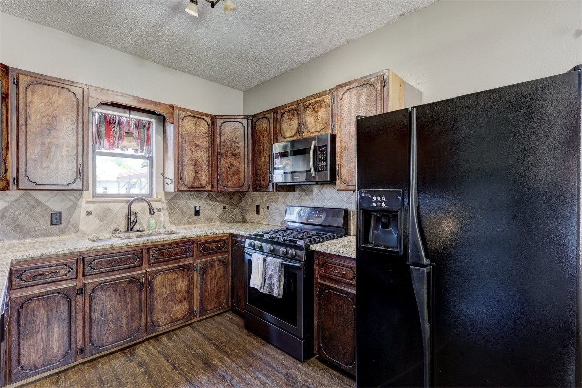 1008 Sunset Drive, El Reno, OK 73036 kitchen featuring dark hardwood / wood-style flooring, black refrigerator with ice dispenser, backsplash, sink, and range with gas cooktop