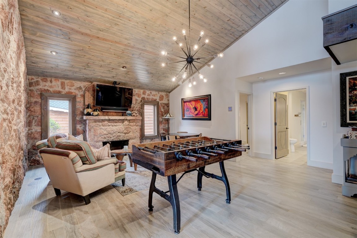 103 E Shore Drive, Arcadia, OK 73007 recreation room featuring a stone fireplace, high vaulted ceiling, a notable chandelier, light hardwood / wood-style floors, and wood ceiling
