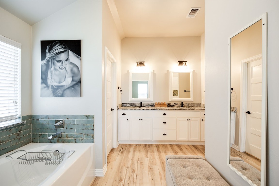 2321 NW 187th Terrace, Edmond, OK 73012 bathroom with vaulted ceiling, a bathing tub, hardwood / wood-style floors, and double sink vanity